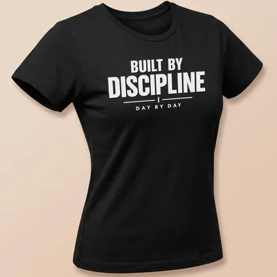 Bold typography shirt with the phrase 'BUILT BY DISCIPLINE DAY BY DAY' in black on white — printed on a women's shirt