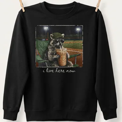 Vintage distressed print of a playful raccoon with the text 'i live here now' — printed on a unisex sweatshirt