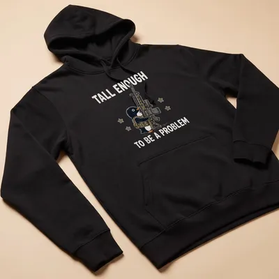 Cartoon penguin with a gun and the text 'Tall Enough To Be A Problem' in black and white — printed on a unisex hoodie
