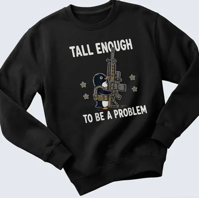 Cartoon penguin with a gun and the text 'Tall Enough To Be A Problem' in black and white — printed on a unisex sweatshirt