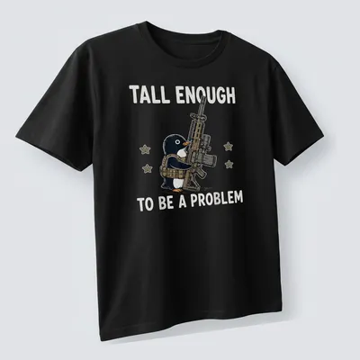 Cartoon penguin with a gun and the text 'Tall Enough To Be A Problem' in black and white — printed on a unisex t-shirt (angled view)
